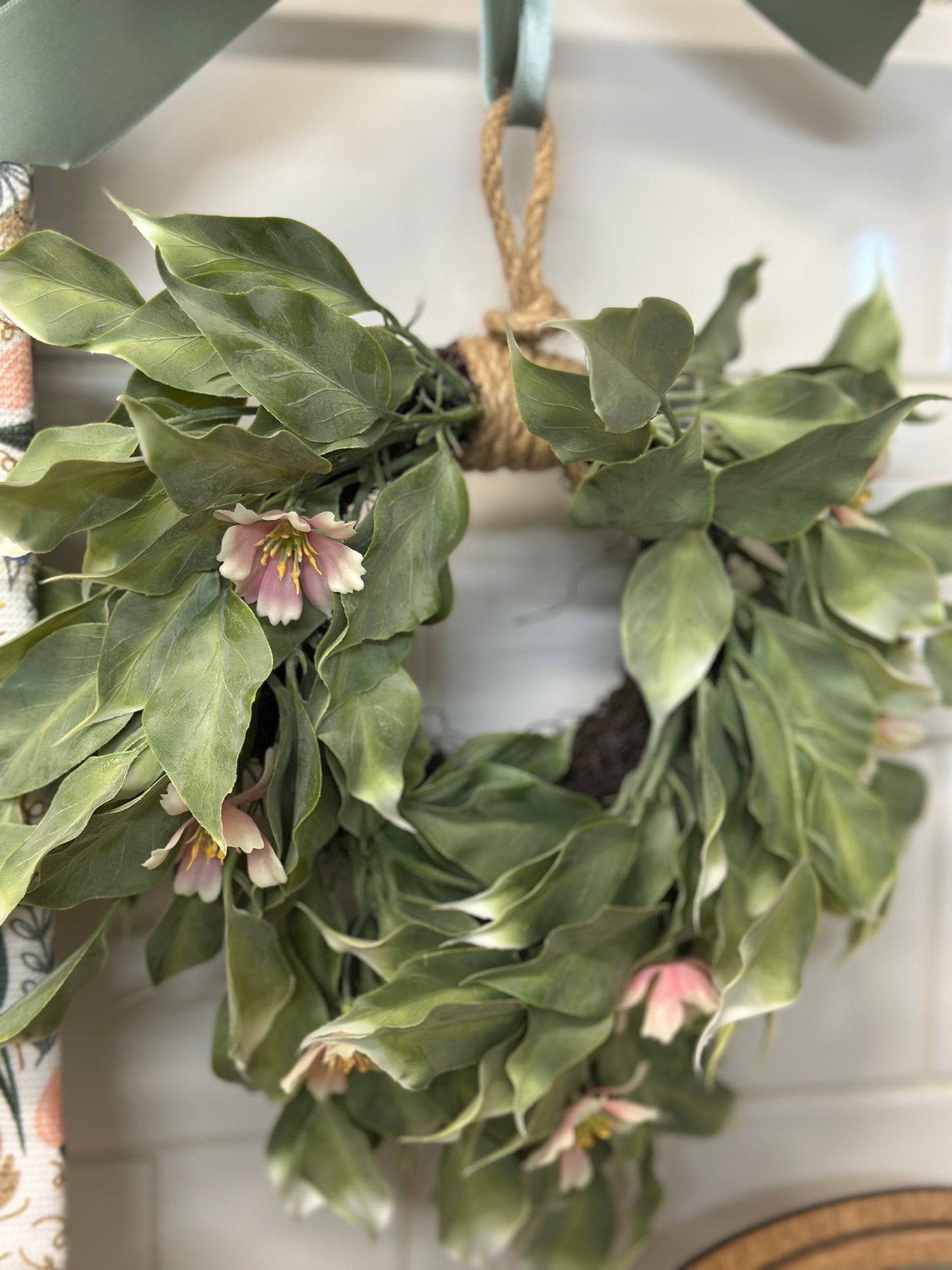 Small Green leafy wreath with small pink flowers hanging on a door, back pr chair on kitchen cabinets