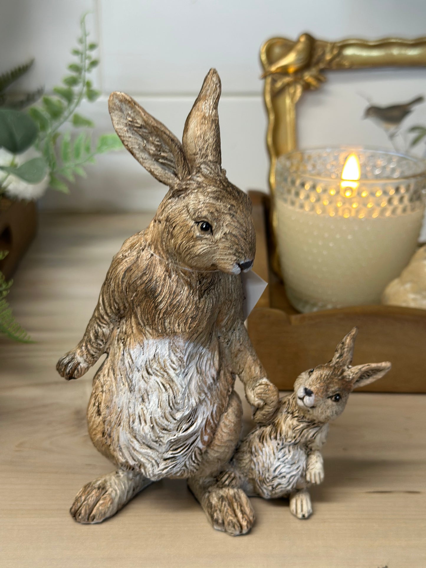 Decorative rabbit statues on a wooden surface with a candle and framed picture in the background.