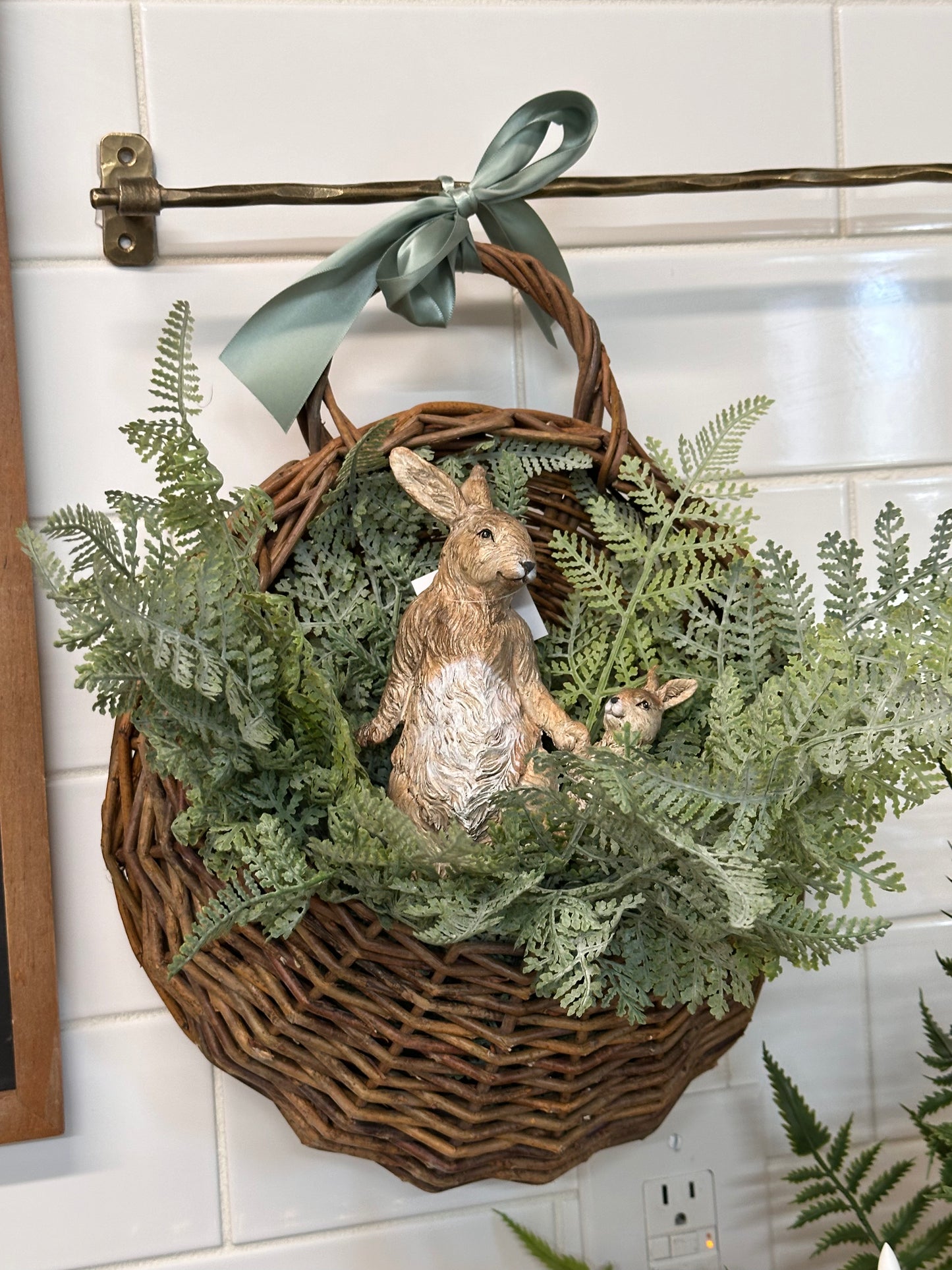 Decorative basket with greenery and a rabbit figurine on a tiled wall.